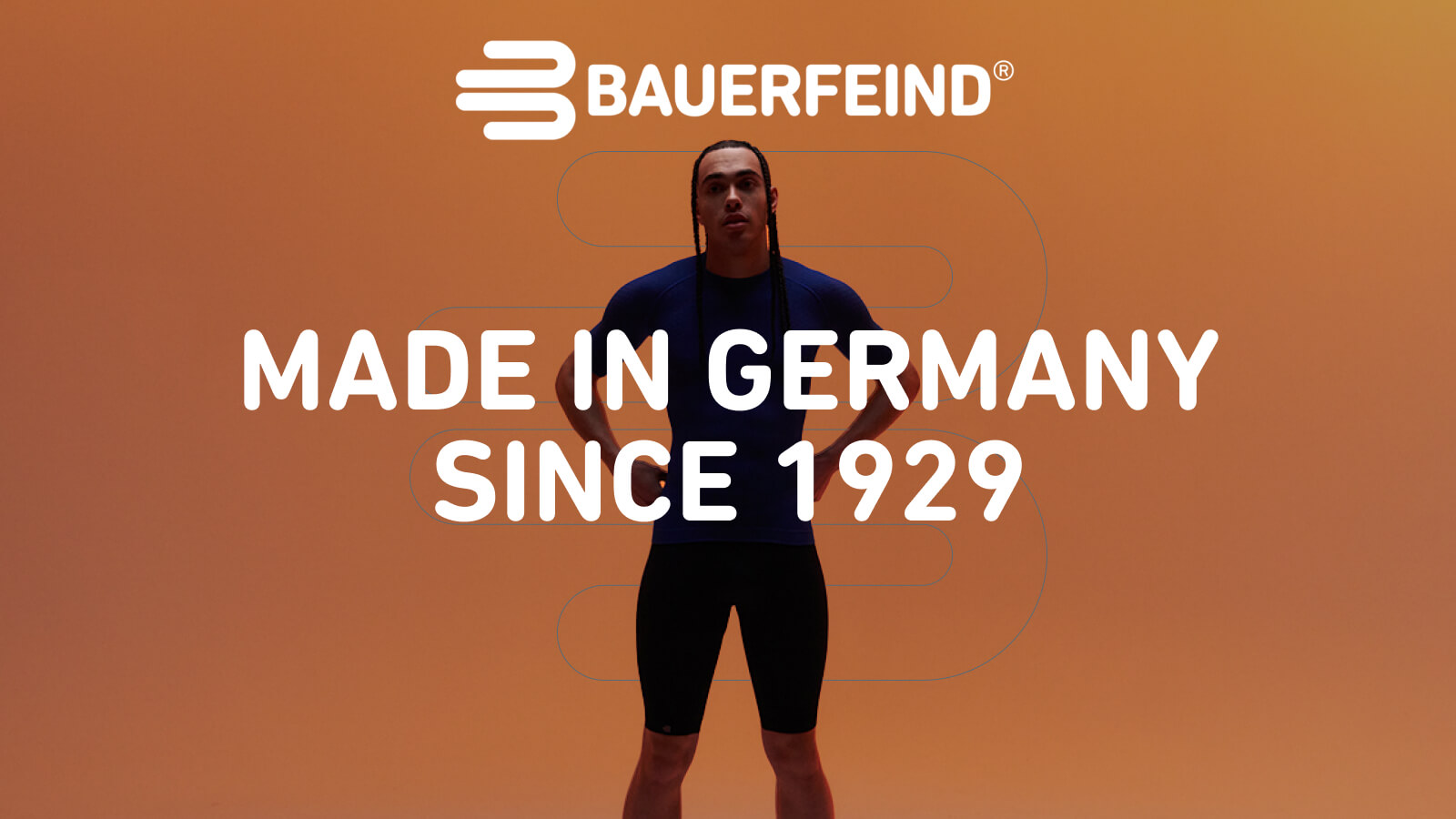 Fiducia con l’abbigliamento compressivo Bauerfeind Una persona è in piedi con le gambe leggermente divaricate davanti a uno sfondo arancione. Indossa una maglia sportiva blu aderente e pantaloncini neri.