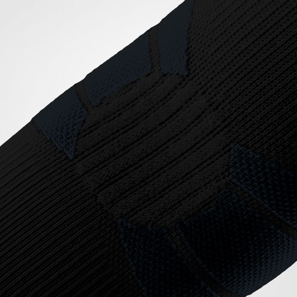 Primo piano della Outdoor Compression Elbow Support nera che avvolge il gomito. La struttura tecnica a maglia con zone di compressione mirate evidenzia la vestibilità anatomica della fascia, progettata per offrire stabilità