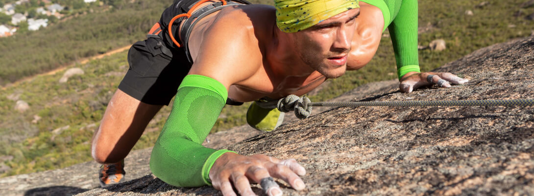 Lo scalatore sulla roccia indossa maniche di compressione verde per il braccio