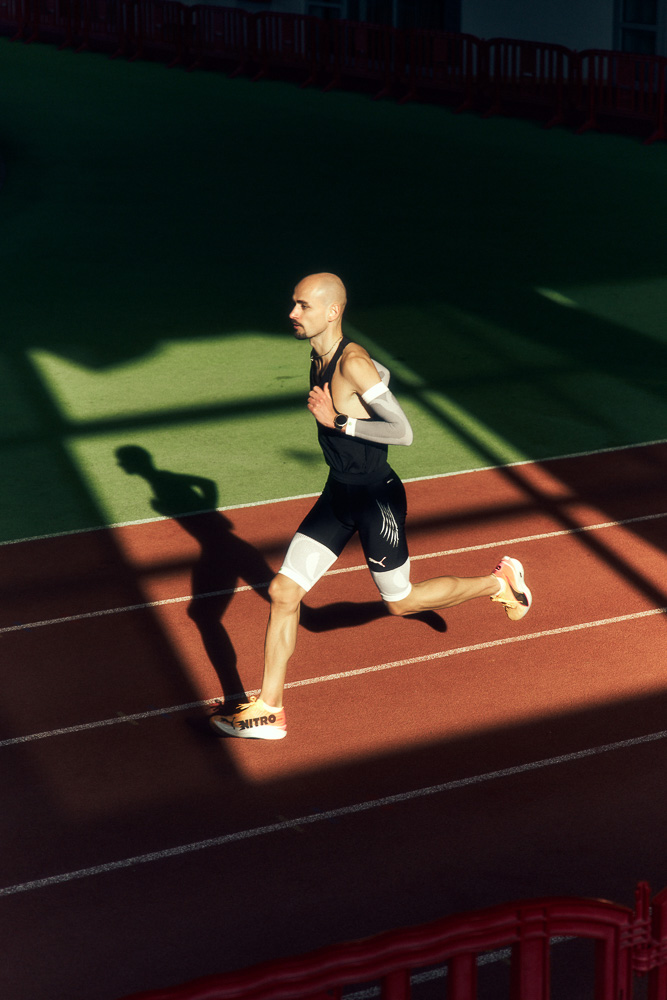 L’atleta professionista Hendrik Pfeiffer corre su una pista indoor con maniche compressive su braccia e gambe per stabilità e performance.