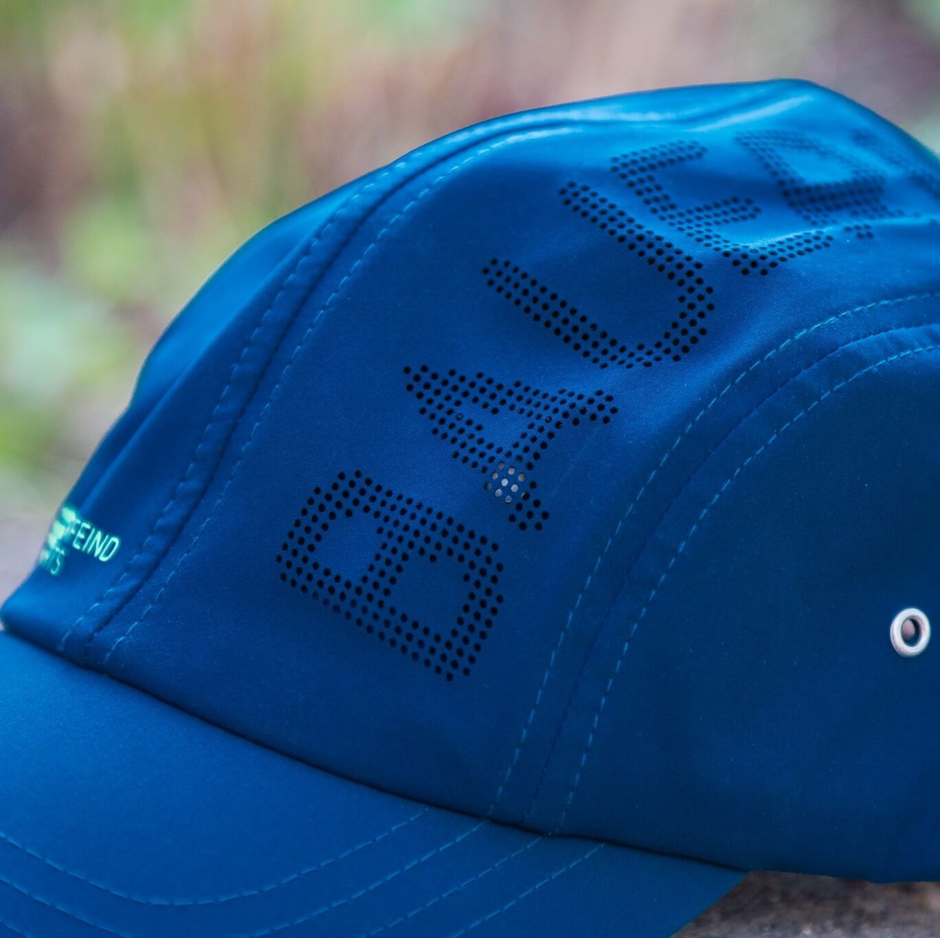 Primo piano del cappellino blu Bauerfeind Sports con scritta BAUERFEIND traforata, cuciture visibili, tessuto tecnico liscio e occhiello metallico laterale – design sportivo pensato per comfort e ventilazione.