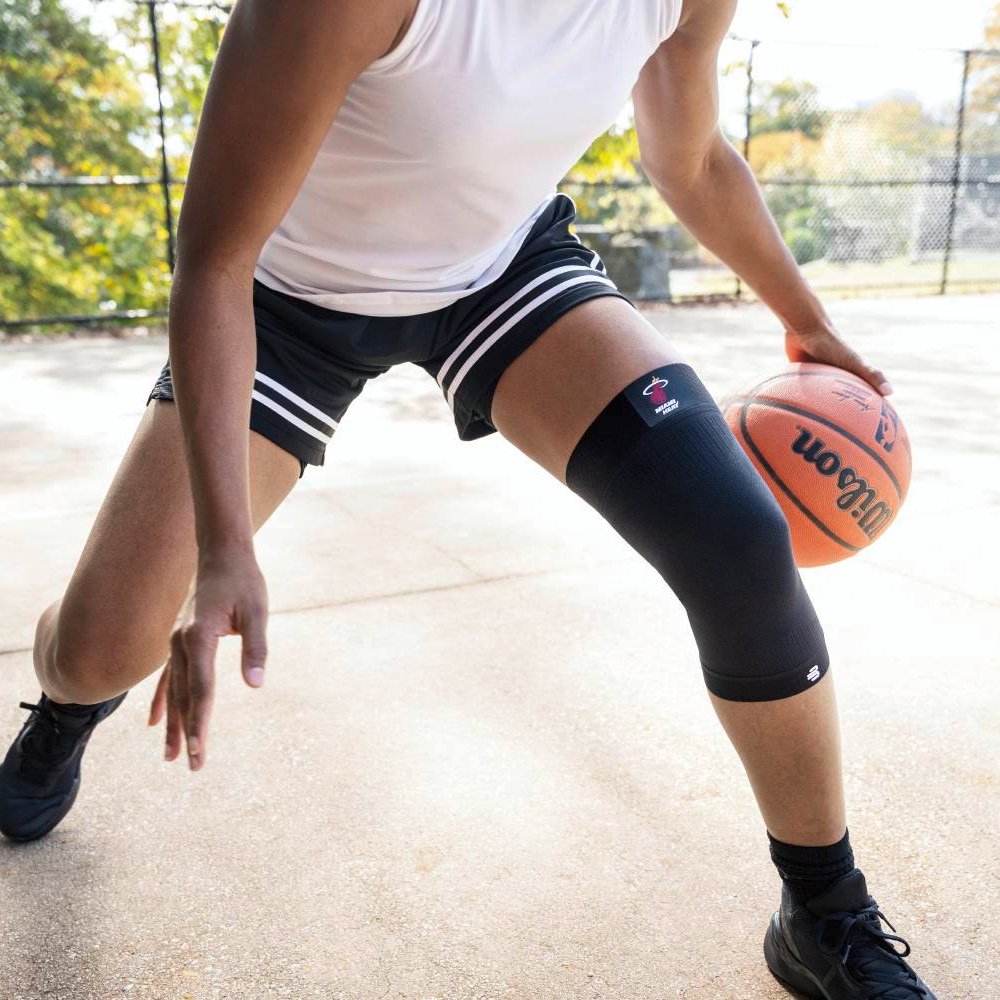 Un giocatore di basket con un supporto per il ginocchio nero dei Miami Heat in difesa. L'attenzione è sulla stabilità del ginocchio nei cambi di direzione rapidi.