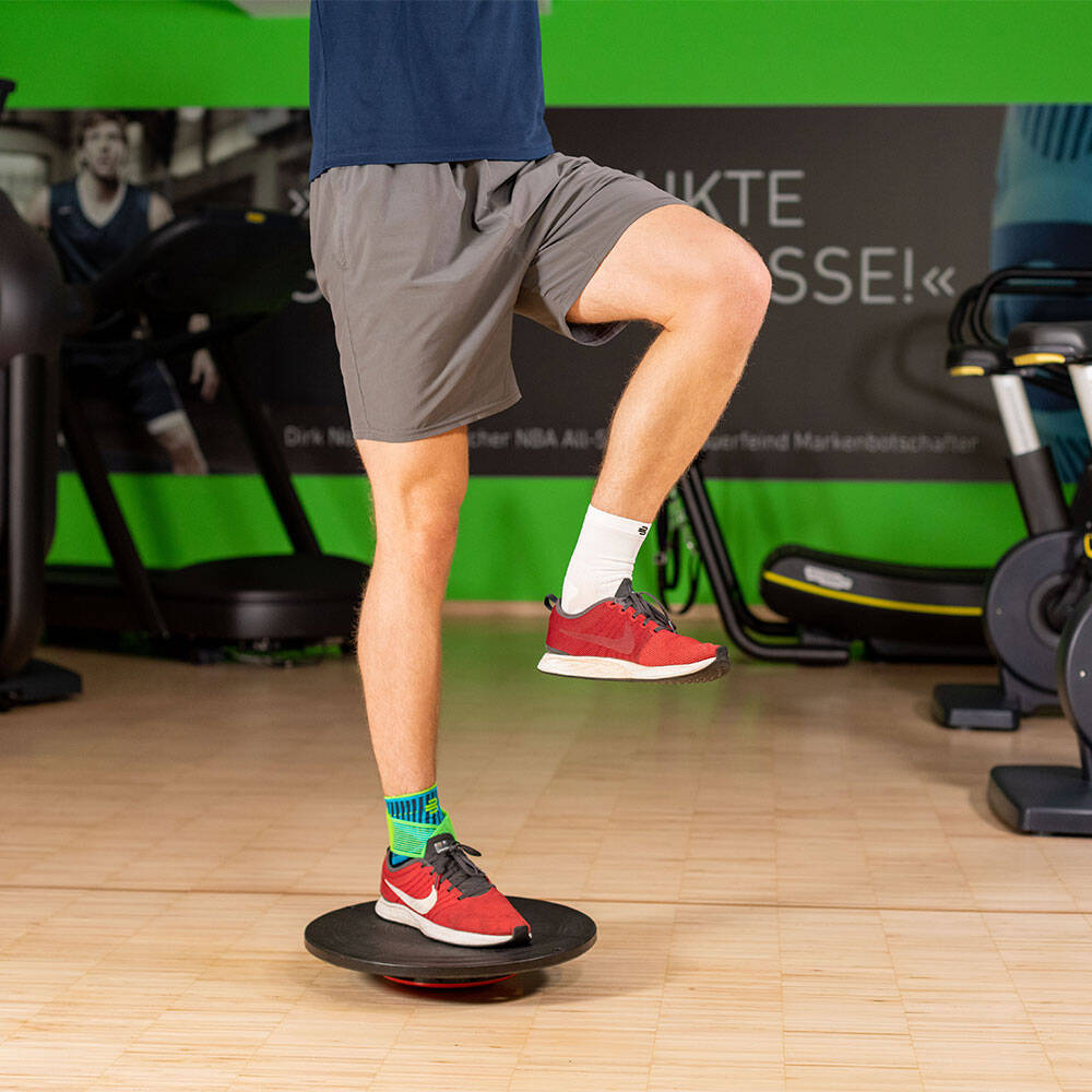 L'uomo in palestra equilibrato con la gamba destra su un bilanciamento e indossa una benda alla caviglia