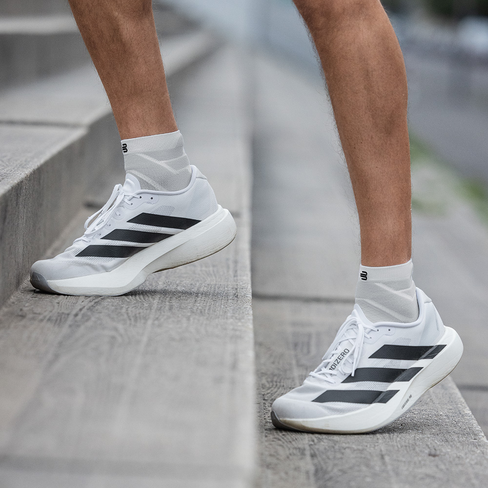 Un uomo è in piedi con le gambe leggermente piegate su una scalinata. Sono visibili i suoi Run Performance Socks corti bianchi e scarpe da corsa bianche con strisce nere.