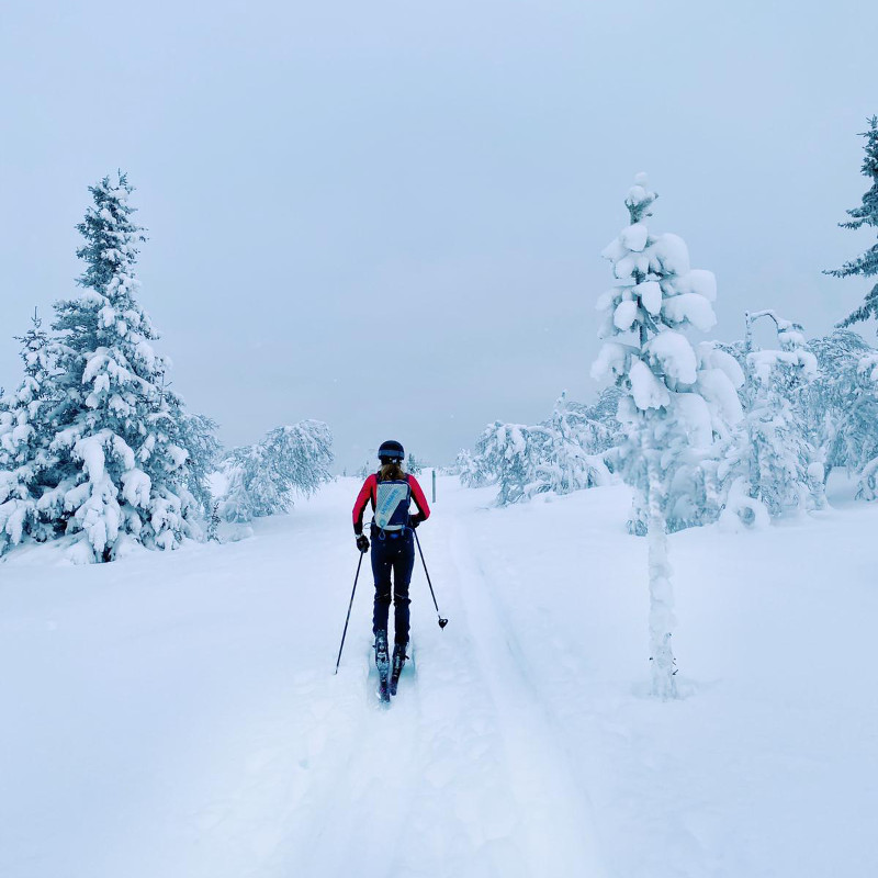 Un lungo corridore con uno zaino si trova di fronte a un paesaggio invernale completamente nevoso