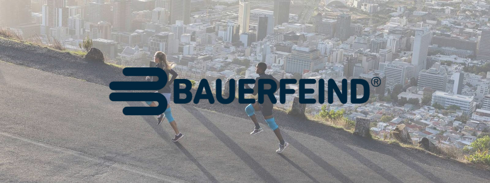 Bauer Enemy Lettering in una foto in cui due corridori corrono su una montagna sopra la città