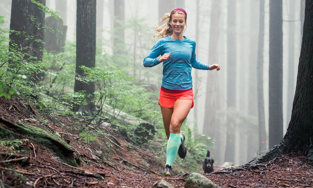 Forest Run with Dog - e le calze a compressione per prestazioni all'aperto La donna corre in lunghe calze all'aperto e con un cane su un sentiero forestale