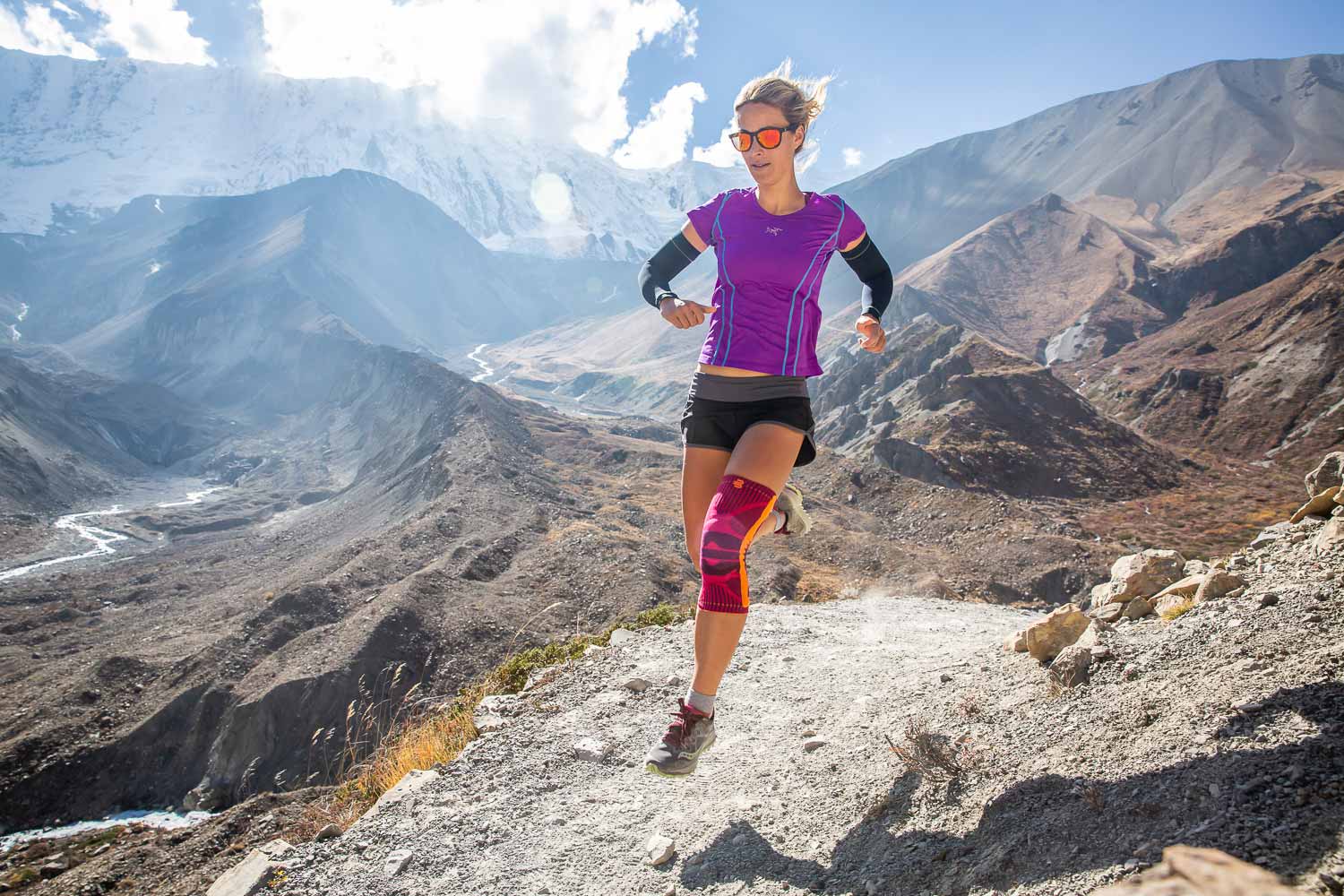 Trekking in Nepal - Hailey van Dyk con supporto sportivo al ginocchio La donna corre attraverso un paesaggio di alta montagna e indossa una ginocchio rosa
