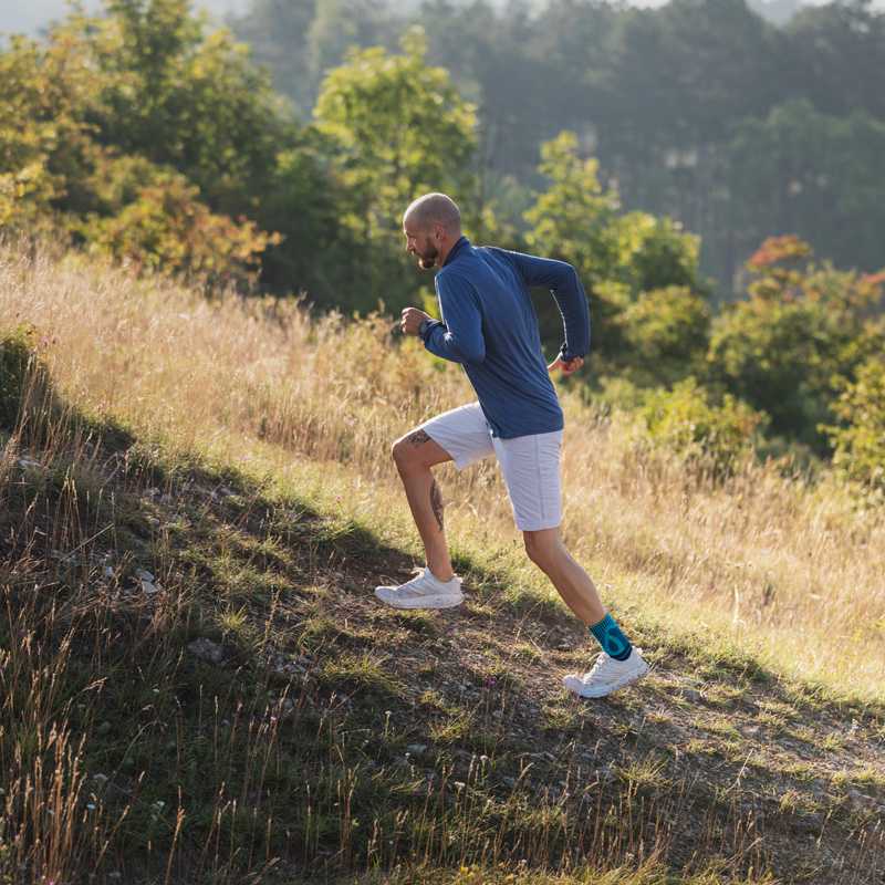 L'uomo corre su una collina con l'erba con una benda del tendine di Achille sul piede