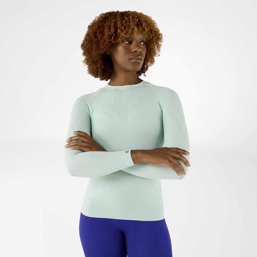 Donna con maglia a maniche lunghe verde chiaro aderente e braccia incrociate, vista frontale