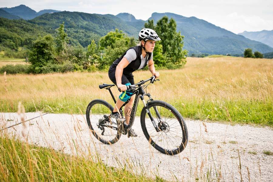 La donna con un ginocchio corre sulla sua mountain bike su un sentiero di ghiaia tra prati e campi