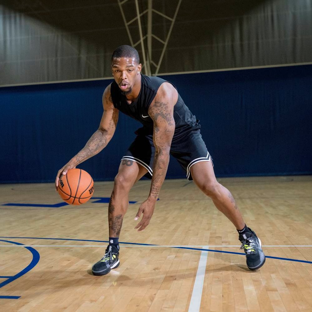 Un giocatore di basket in abbigliamento sportivo nero palleggia sul campo. Indossa la Bauerfeind Sports Ankle Support in nero sulle caviglie.
