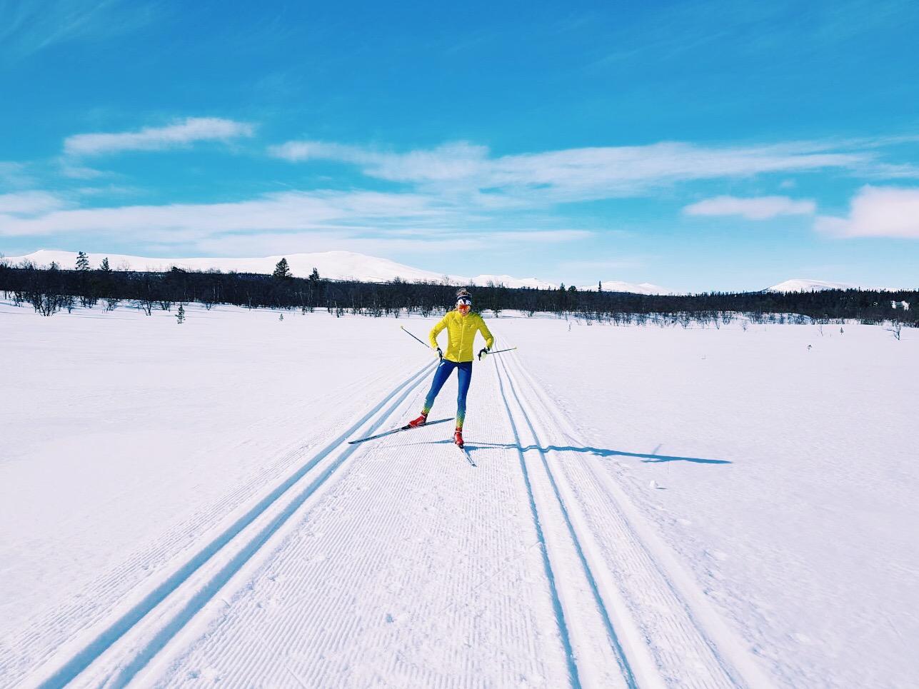Un lungo corridore in una giacca gialla al doppio ritorno tra due sentieri nel paesaggio invernale con un cielo blu