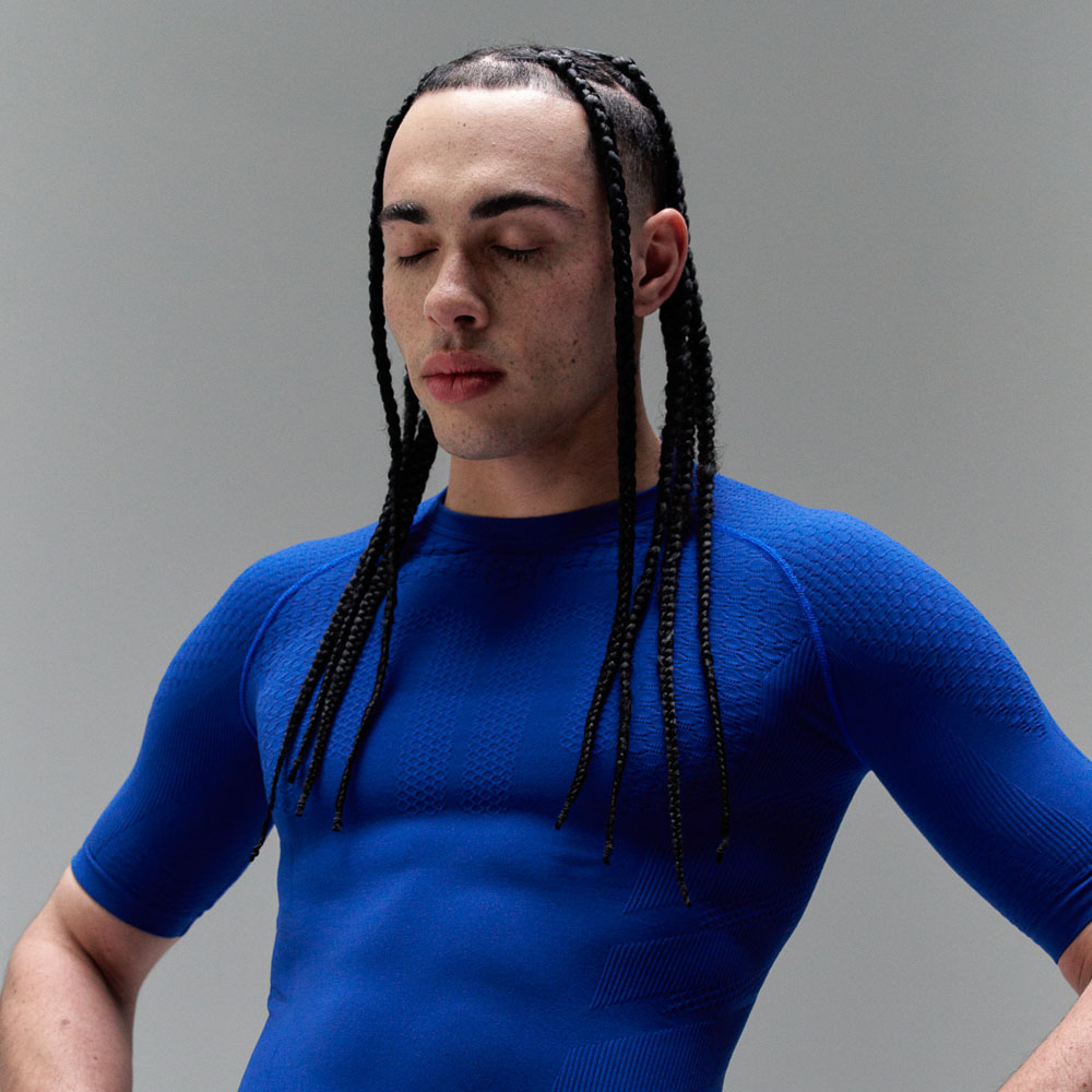 Un uomo con le trecce indossa un top sportivo blu scuro, che mette in risalto i suoi muscoli.