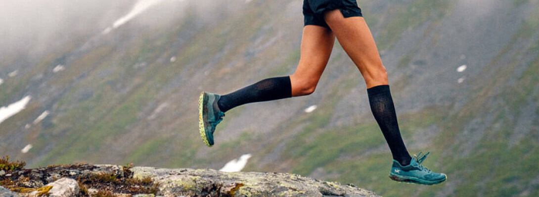 Corridore con calzini neri a compressione leggera per correre su un sentiero di fronte a una montagna