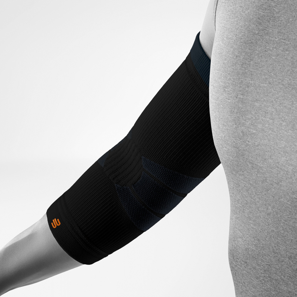 Vista angolata della Outdoor Compression Elbow Support nera su avambraccio e gomito. La fascia compressiva evidenzia le zone di supporto anatomiche e il logo integrato nella parte inferiore.
