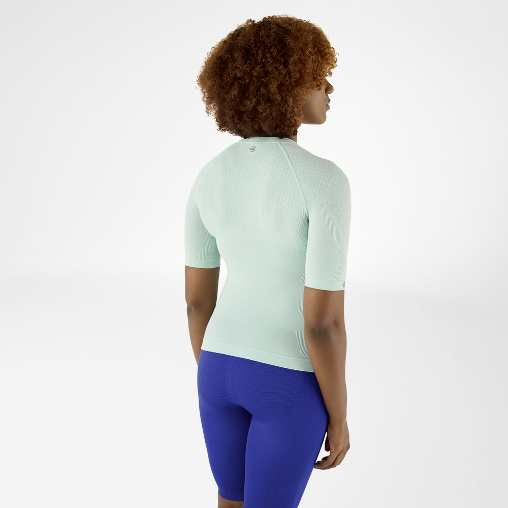Vista posteriore di una donna con capelli ricci in una maglia a compressione verde menta e leggings blu, che guarda leggermente di lato.