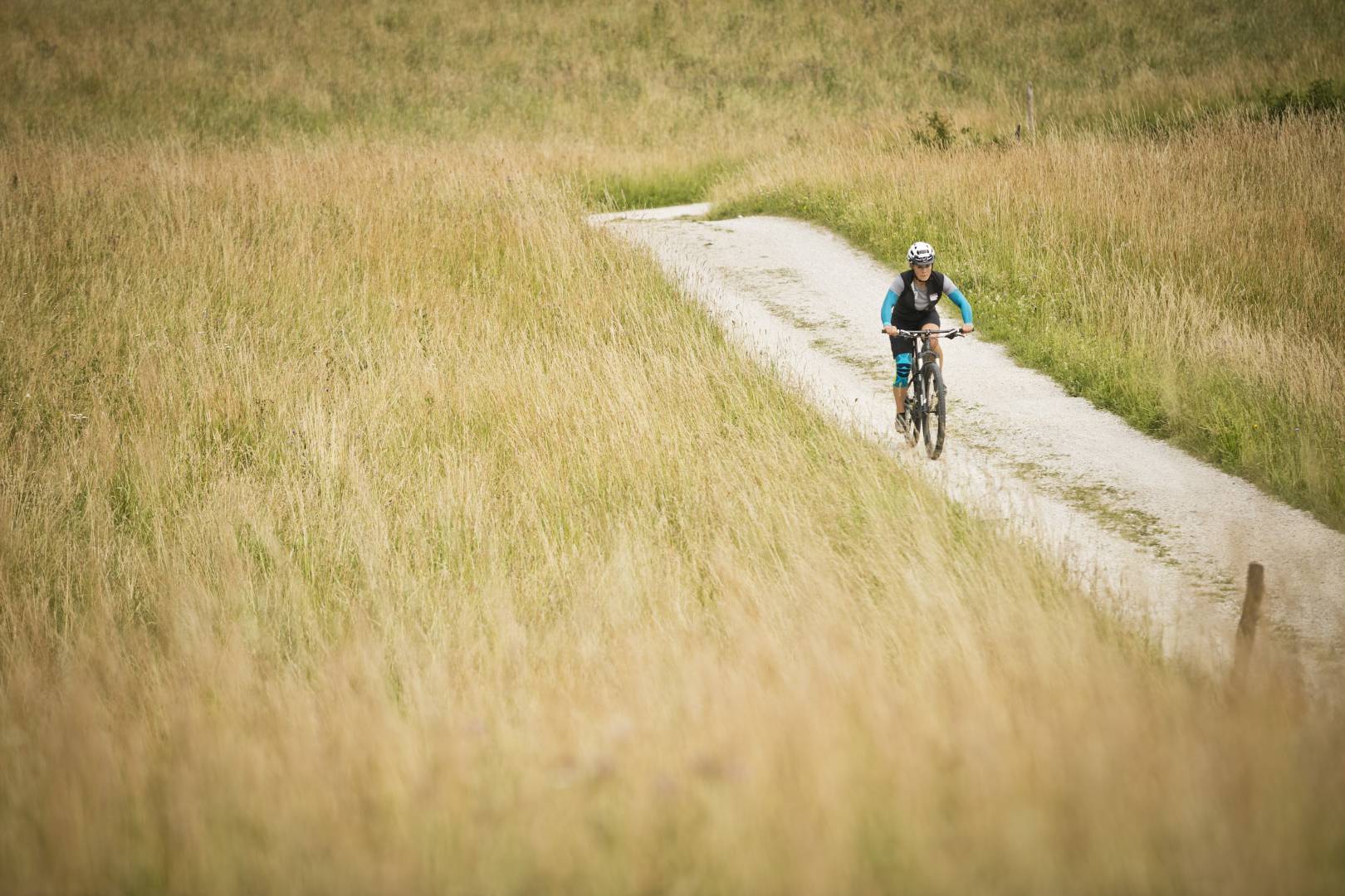Donna con armi e fascette sullo sfondo dell'immagine corre su una mountain bike su un sentiero tra l'erba alta