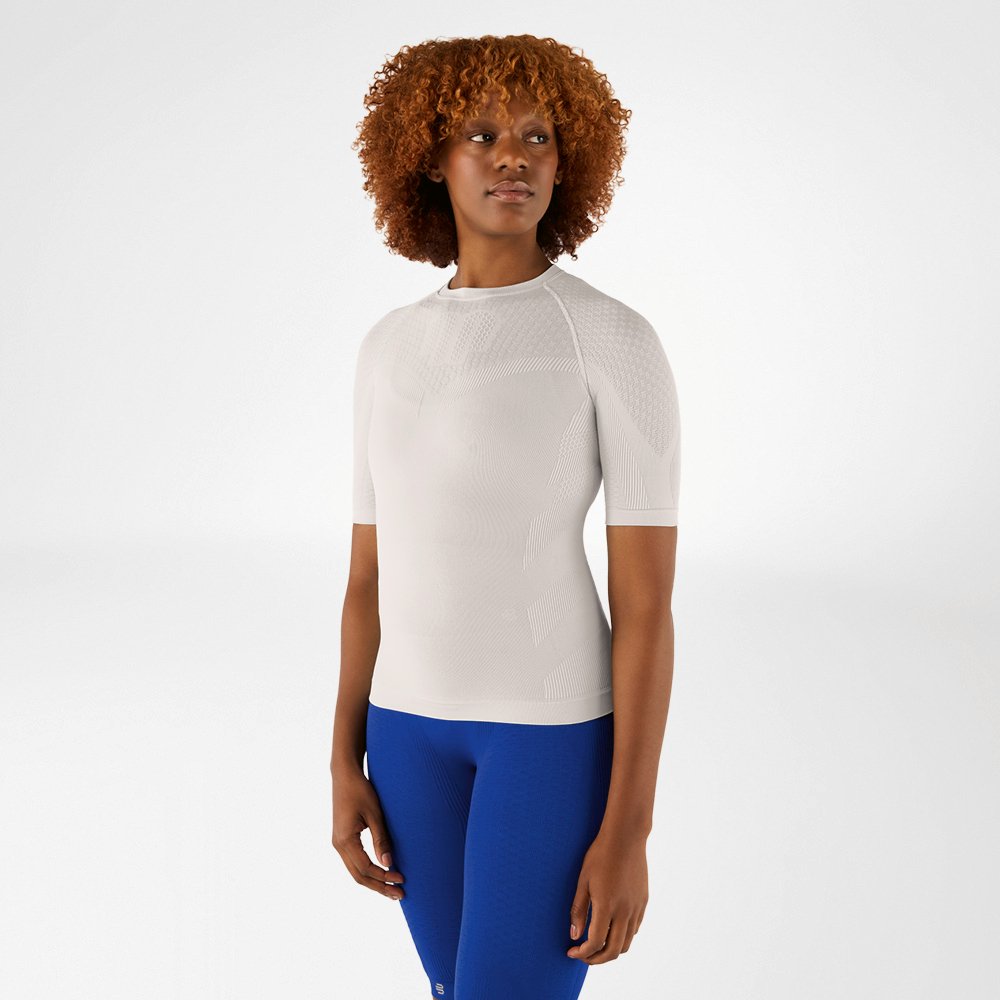 Donna con capelli ricci indossa una maglia a compressione grigio argento e leggings blu. È in piedi rivolta in avanti e guarda di lato.