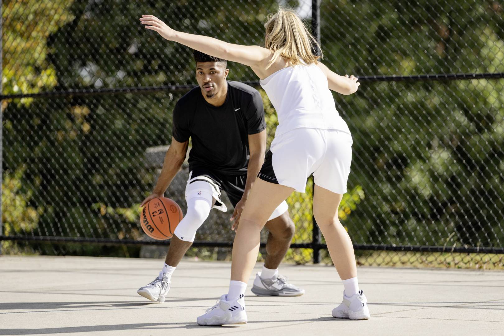 Giocatore di streetball con manica al ginocchio bianco cerca di superare un avversario che lo sta aspettando con le braccia sparse fuori