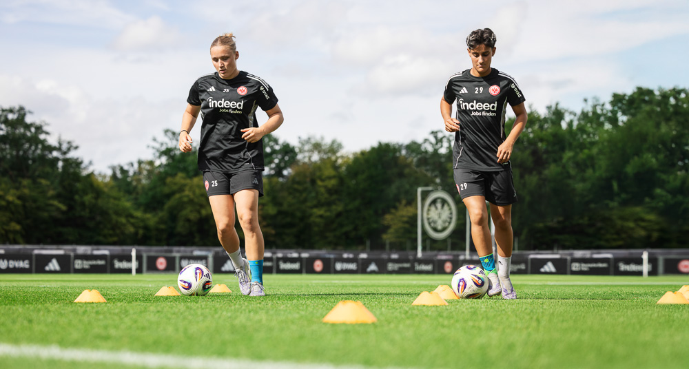 Due giocatrici dell’Eintracht Francoforte si allenano con coni e pallone sul campo, indossando tenute nere da allenamento. Entrambe utilizzano prodotti compressivi Bauerfeind Sports, perfetti per movimenti dinamici.