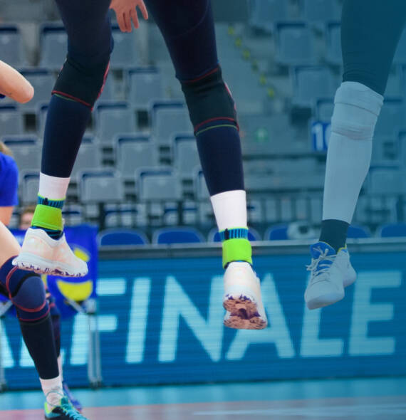 Giocatore di pallavolo con pantaloni scuri scarpe bianche e bende alla caviglia blu "stand" in aria