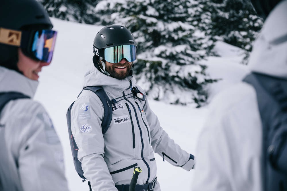 Bello, skier bene con una giacca grigia del casco nero e una registrazione dello zaino tra altri due sciatori