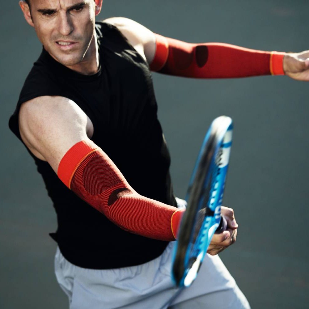 Un tennista con maniche a compressione rosse colpisce la palla con intensa concentrazione.