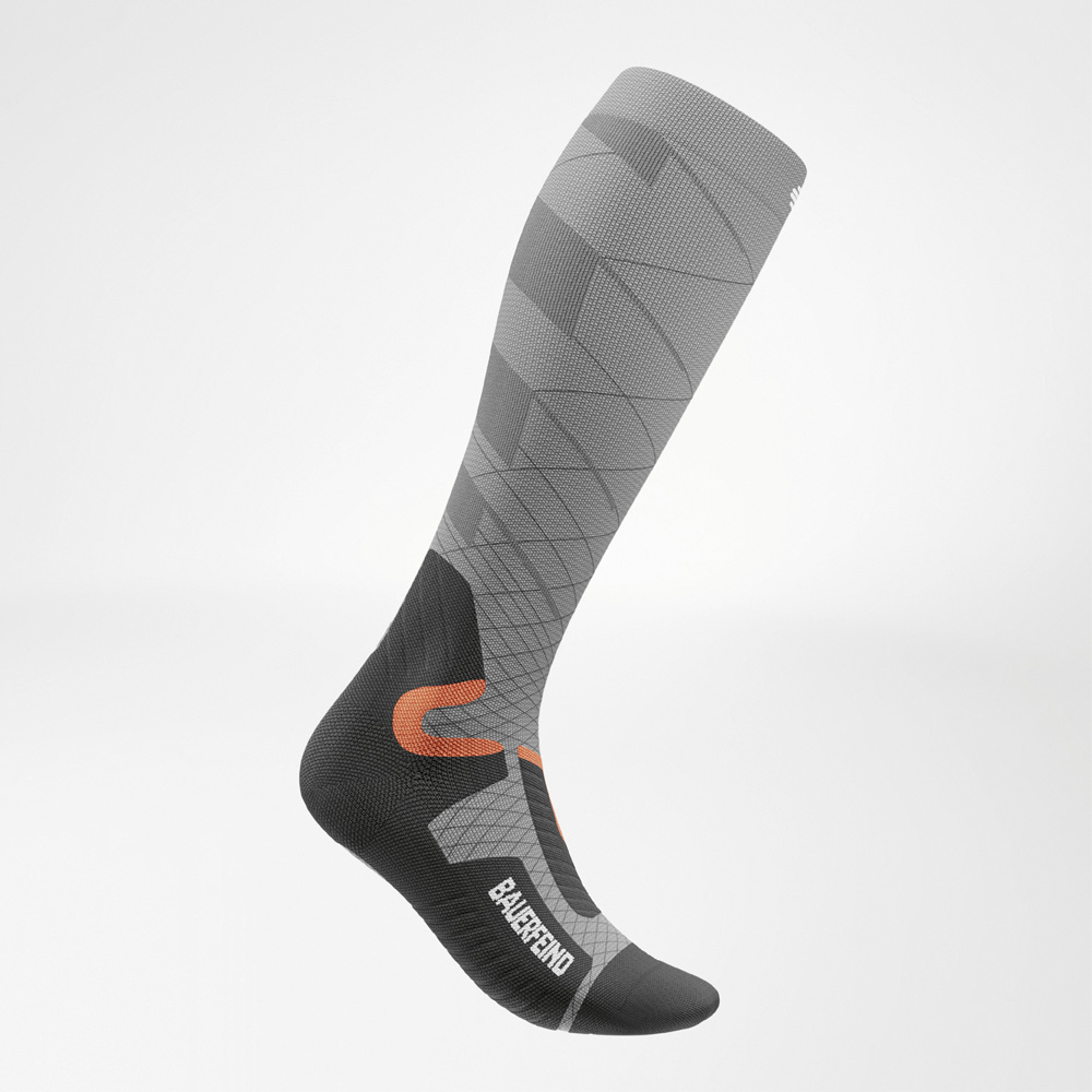 Calza da sci compressiva da donna in grigio vista laterale, con vestibilità anatomica ottimizzata e dettagli arancioni e neri dal look sportivo.