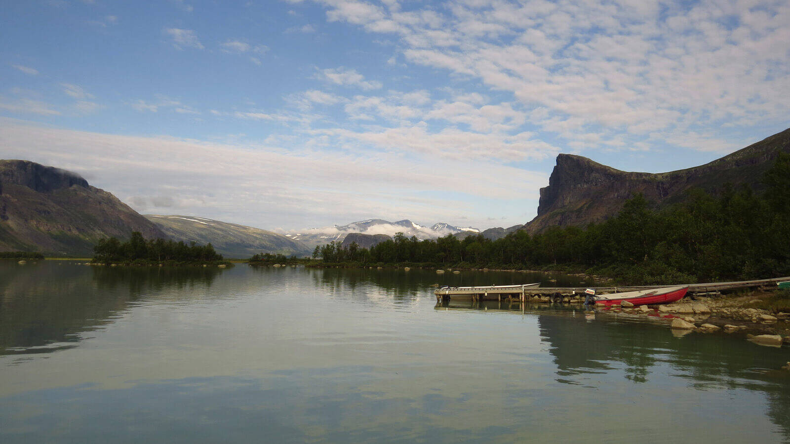 Panorama di un lago circondato da alberi e piccole montagne sul bordo destro è una piccola barca sul molo