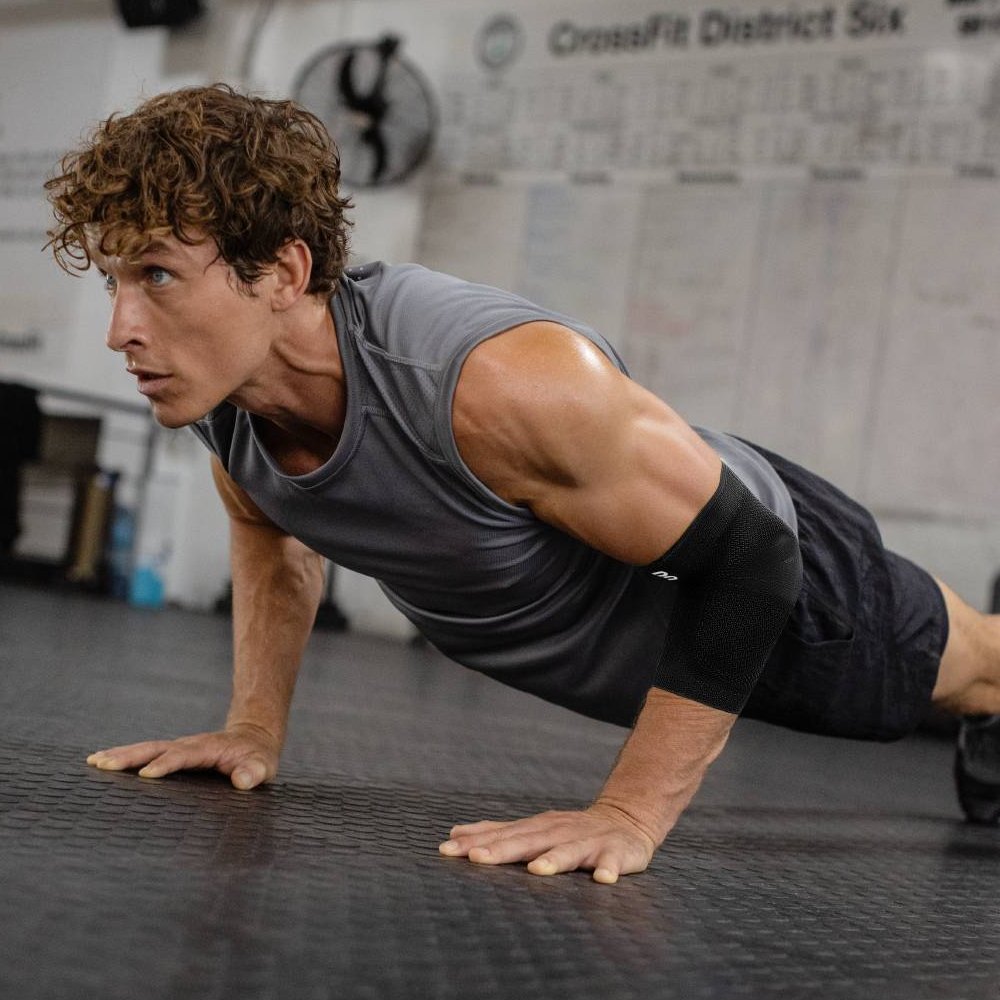Un atleta in palestra durante un intenso allenamento di piegamenti, che indossa una fascia per il gomito nera. La fascia fornisce supporto stabile e protezione ottimale per il gomito durante l'allenamento di forza e le sfide sportive.