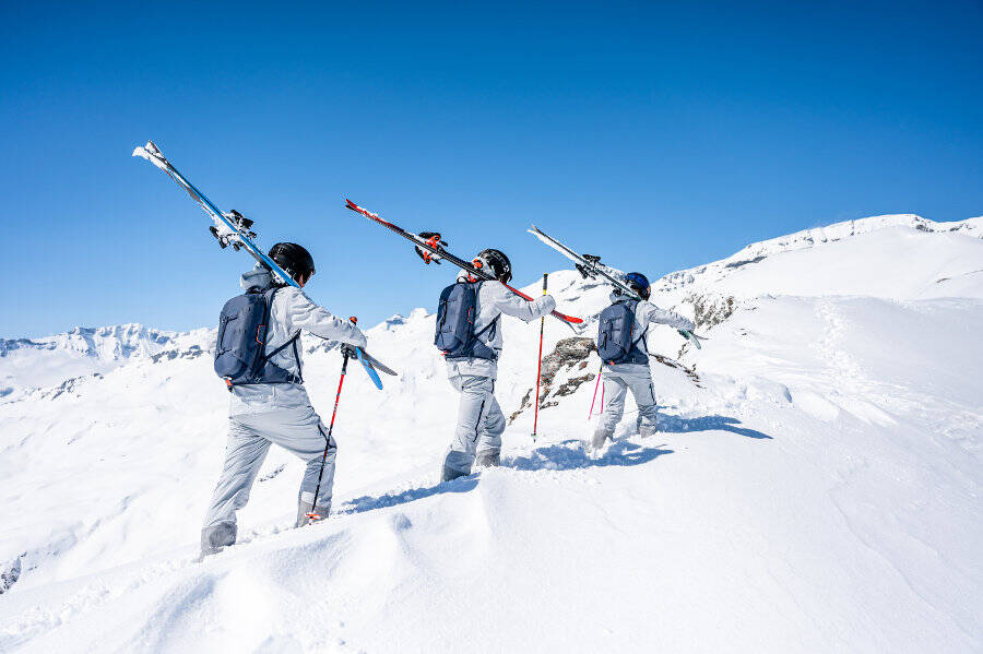 Tre sciatori portano i loro sci sulle spalle attraverso la neve profonda su una montagna