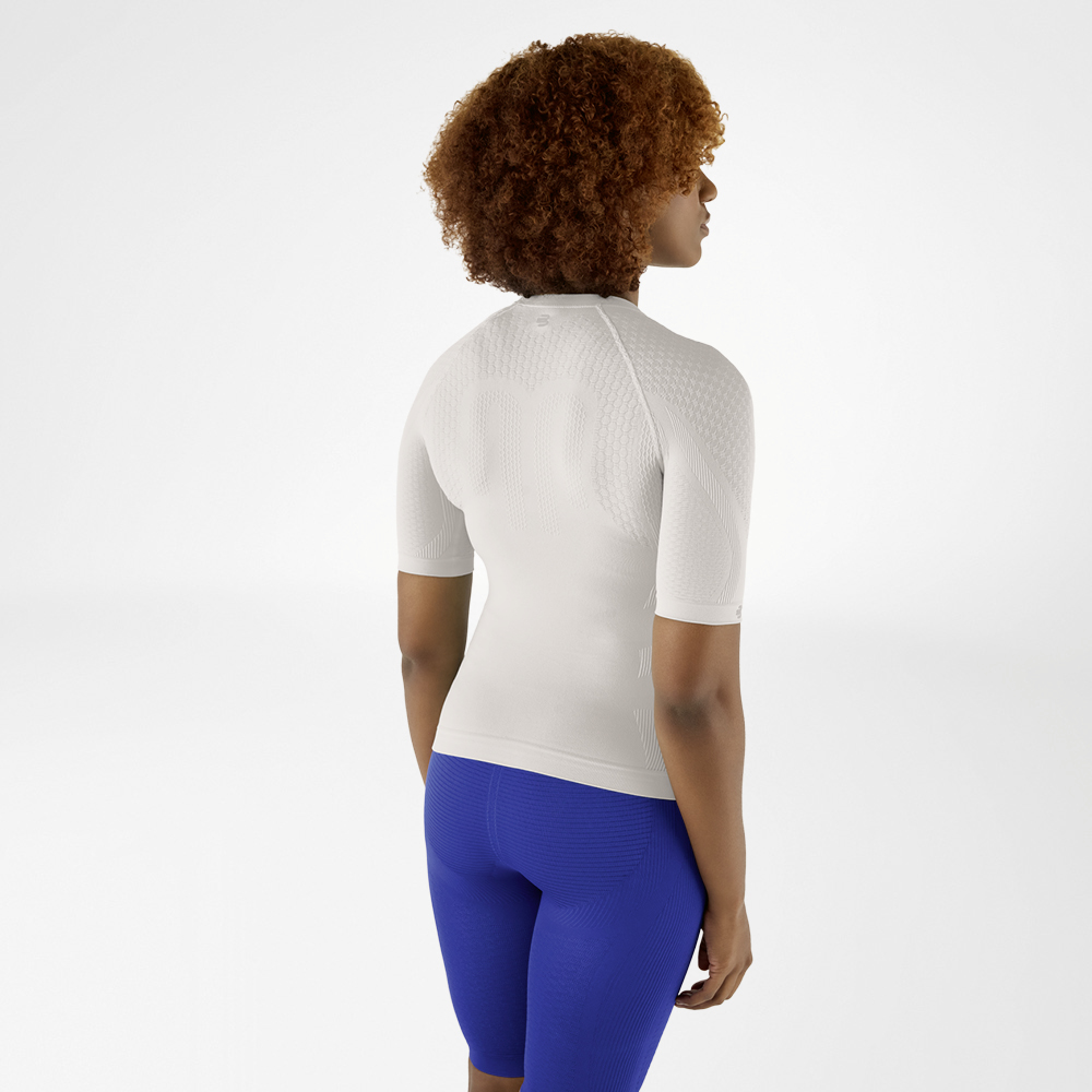 Vista posteriore di una donna con capelli ricci in una maglia a compressione grigio argento e leggings blu, che guarda leggermente di lato.