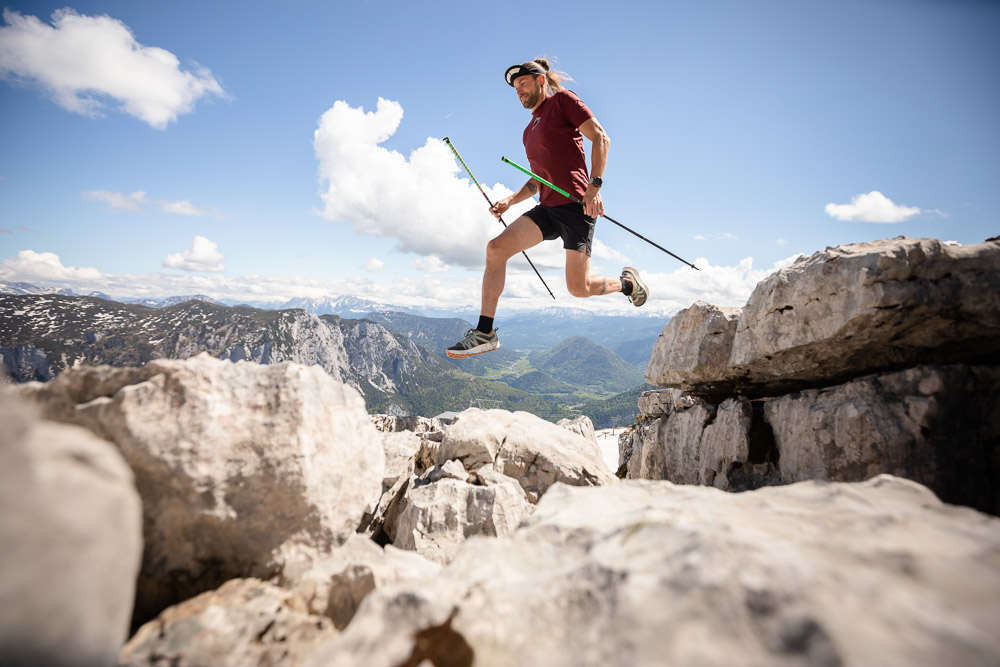 Lord Jens Kramer durante il trail running con bastoncini mentre salta tra le rocce in alta montagna