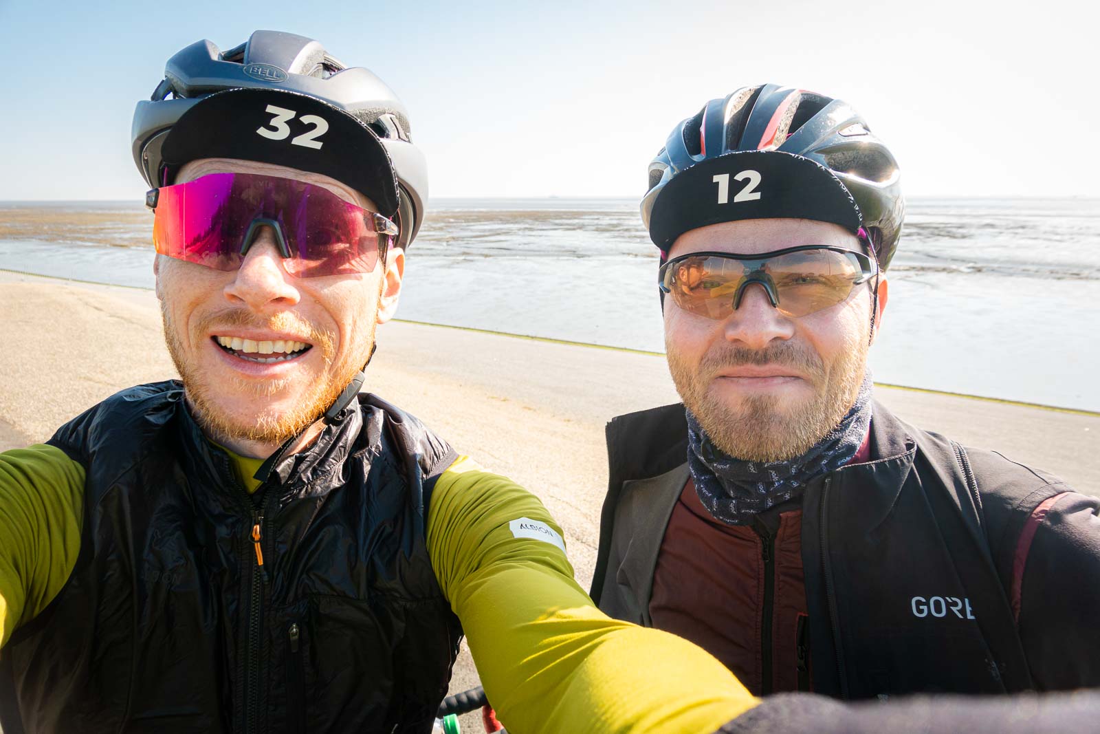 Due ciclisti si scattano un selfie davanti al panorama di una spiaggia e ridono.