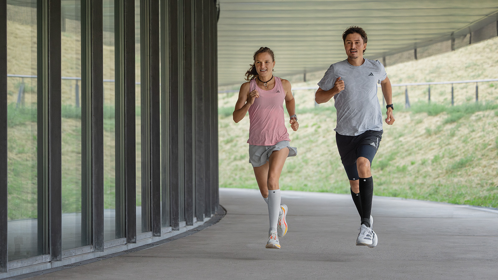 Dai il gas e divertiti: con i nostri calzini a compressione perfoma run Langer con i calzini da corsa rosa bianca corre accanto a un muro moderno